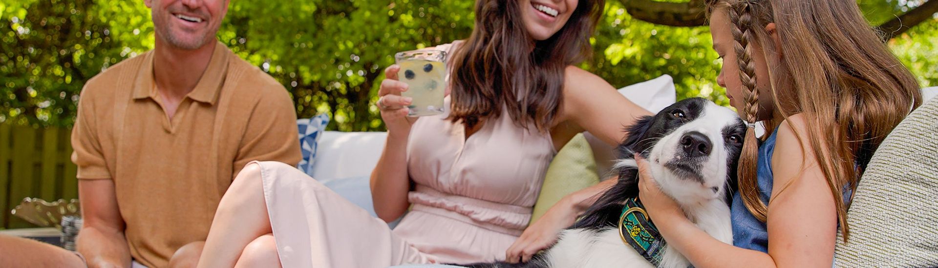 Happy family in a garden scene, playing with their dog on an outdoor sofa